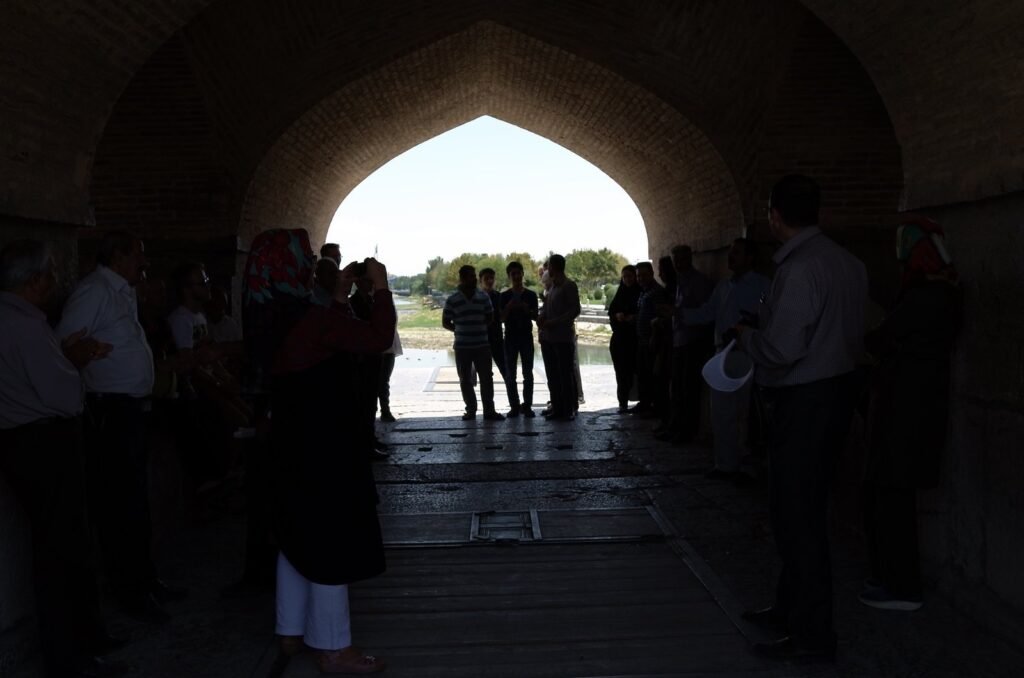 Tour group in the shade under an arch of a historic bridge in Isfahan
