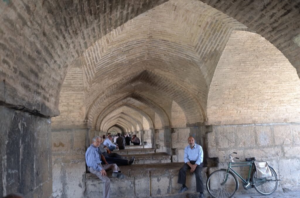 Men and a bicycle under the long stone arches of a bridge in Isfahan