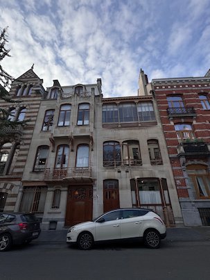 An Art Nouveau townhouse with a large window stands on a street in Brussels.