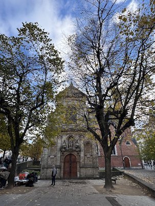 A baroque church stands behind two tall trees on a square in Brussels.