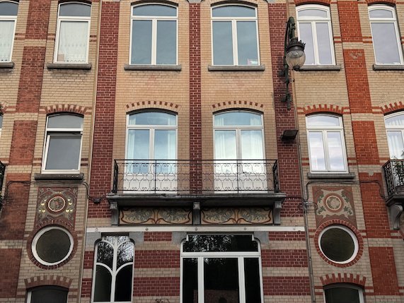 A brick facade with round windows and iron balconies stands in Brussels.
