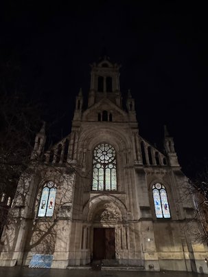 A church facade with a rose window stands in the dark in Brussels.
