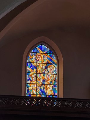 A modern stained glass window with bright colors sits above a balcony in a church in Brussels.