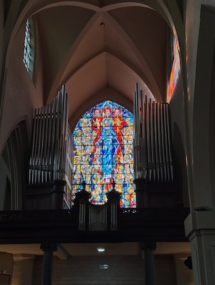 A colorful window shines between organ pipes in a church in Brussels.