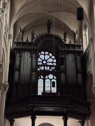 A dark wooden organ stands below a rose window in a church in Brussels.