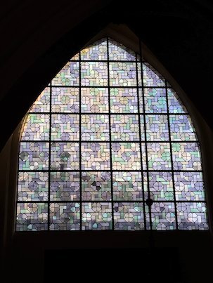 A large pointed window with pale glass squares fills a church wall in Brussels.