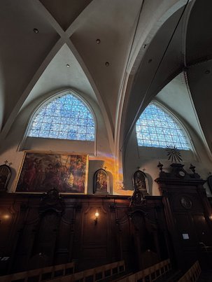Light windows shine above dark paintings and wood panels in a church in Brussels.