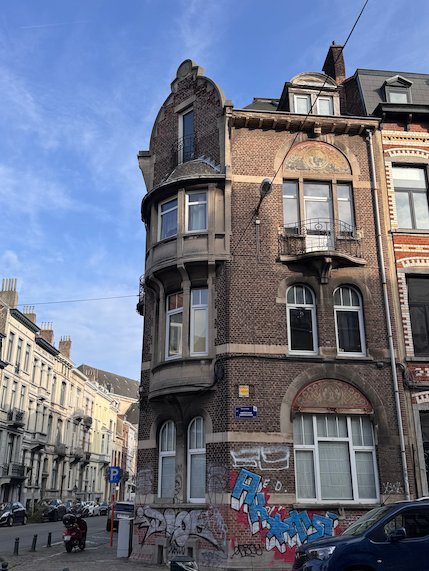 A brick corner house with a round bay window stands on a street in Brussels.