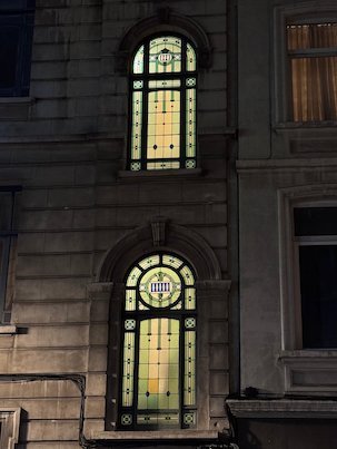 Lit stained glass windows shine in an old building at night in Brussels.