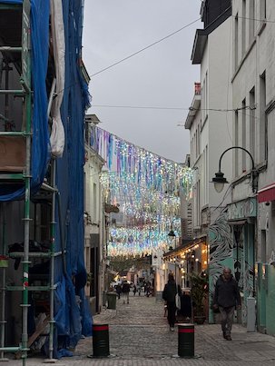 Colorful decorations hang above a narrow street with shops in Brussels.
