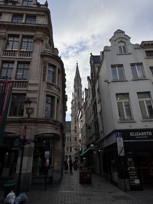A narrow street leads toward the spire of the Town Hall in Brussels.
