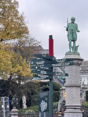 A bronze statue on a column stands next to a signpost at the Petit Sablon in Brussels.