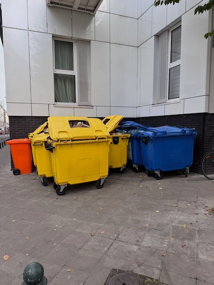 Yellow, blue and orange recycling bins stand next to a building in Brussels.