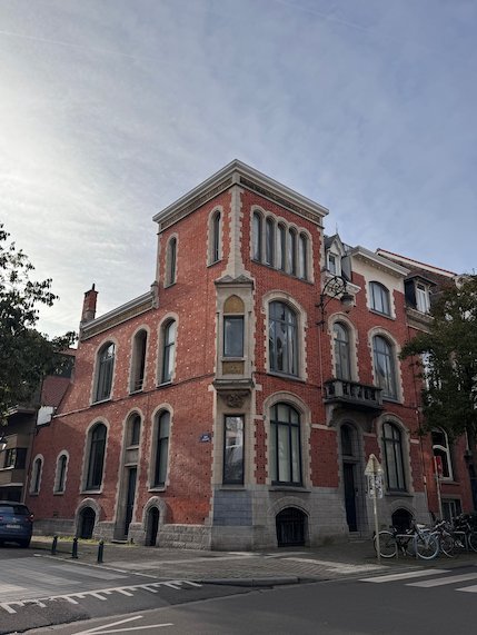 A red brick mansion with tall windows stands on a street corner in Brussels.
