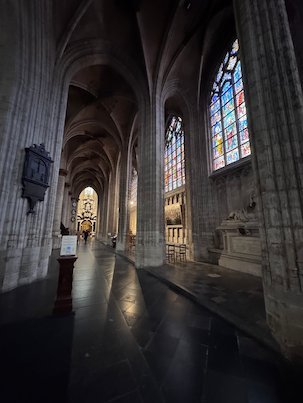 Colorful windows light a dark side aisle of the Sablon church in Brussels.