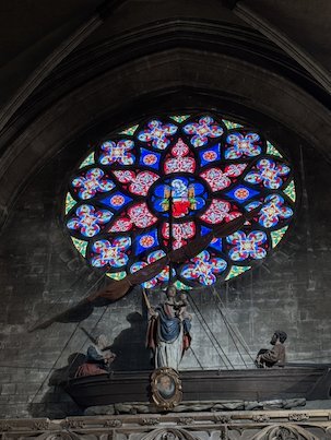 A boat with statues hangs below a colorful rose window in the Sablon church.