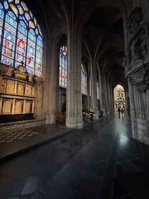 Tall stained glass windows line a side aisle of the Sablon church in Brussels.