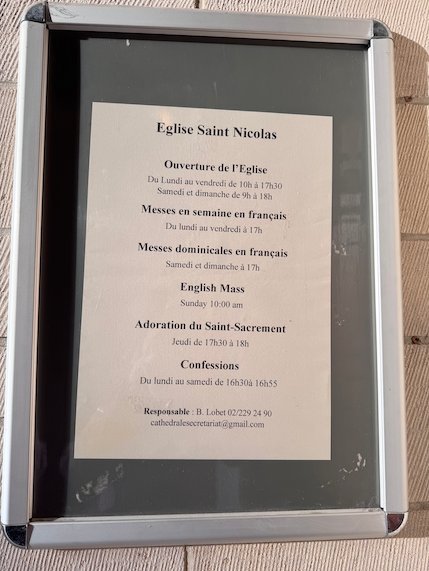 A sign gives the opening hours and mass times of the Church of Saint Nicholas.