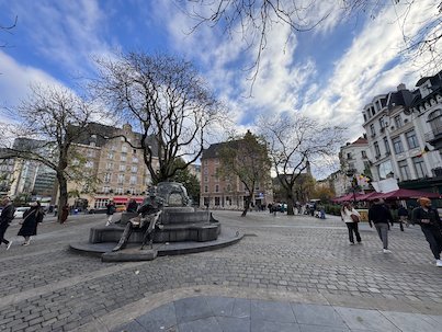 A statue stands on a square with bare trees and cafes in Brussels.