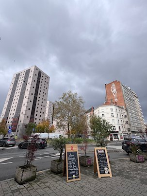 Tall tower blocks stand next to a street with cafe signs in Brussels.