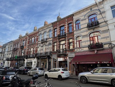 A row of old townhouses with shops and balconies lines a street in Brussels.