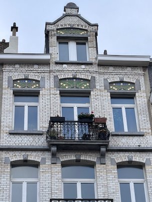 A white brick townhouse with an iron balcony stands on a street in Brussels.