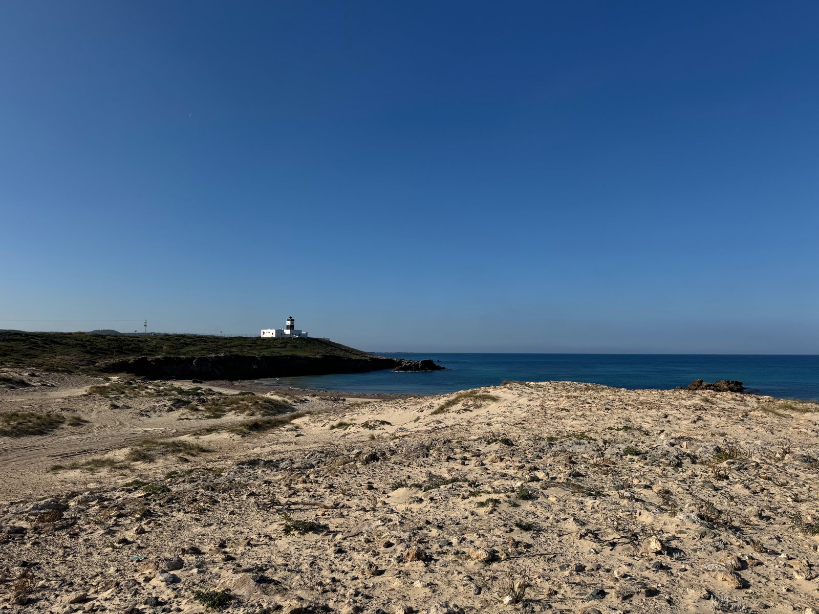 The white lighthouse of Cap Angela stands on a green headland across a blue bay near Bizerte, Tunisia.