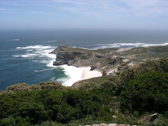 The rocky Cape of Good Hope reaches into the Atlantic Ocean behind green bush, South Africa.