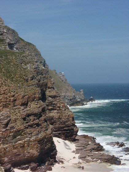 Steep brown cliffs drop into blue sea and white surf at Cape Point near Cape Town.