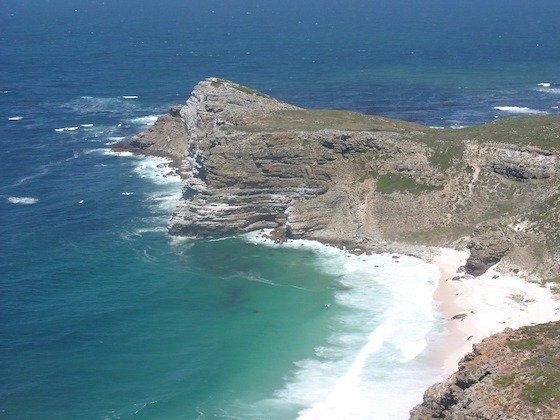 Green cliffs and a white sandy bay meet blue sea at Cape Point on the Cape Peninsula.