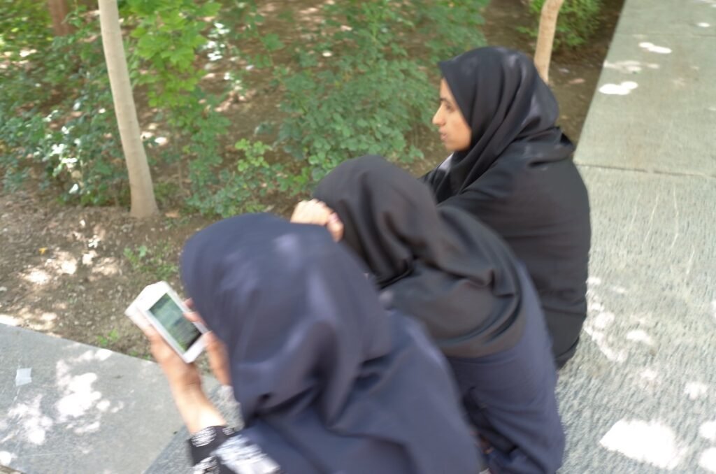 Women in black scarves look at a phone in the Chehel Sotoun garden