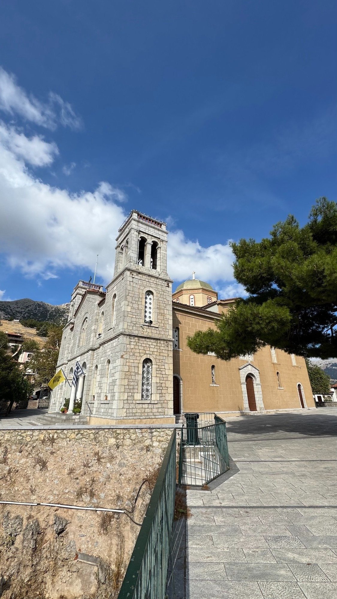 Stone church with a bell tower beside a pine tree in a village near Delphi