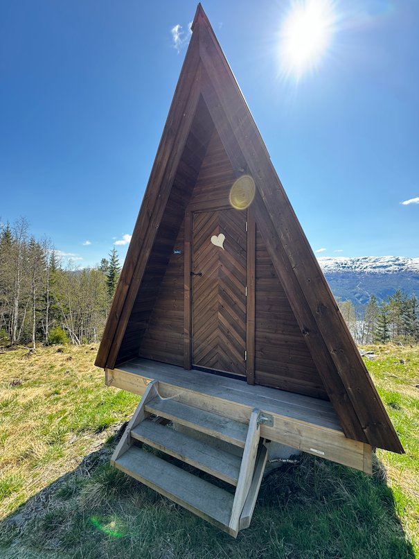 Small A-frame outhouse with a heart on the door near Dagsturhytta, with mountains behind