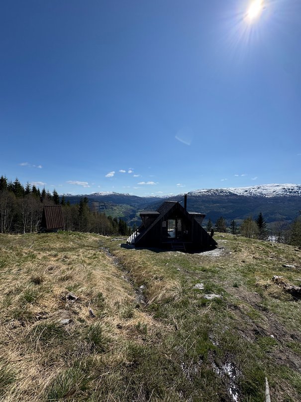 Dagsturhytta, a black A-frame day-trip cabin on a hill above Voss, with snowy mountains behind