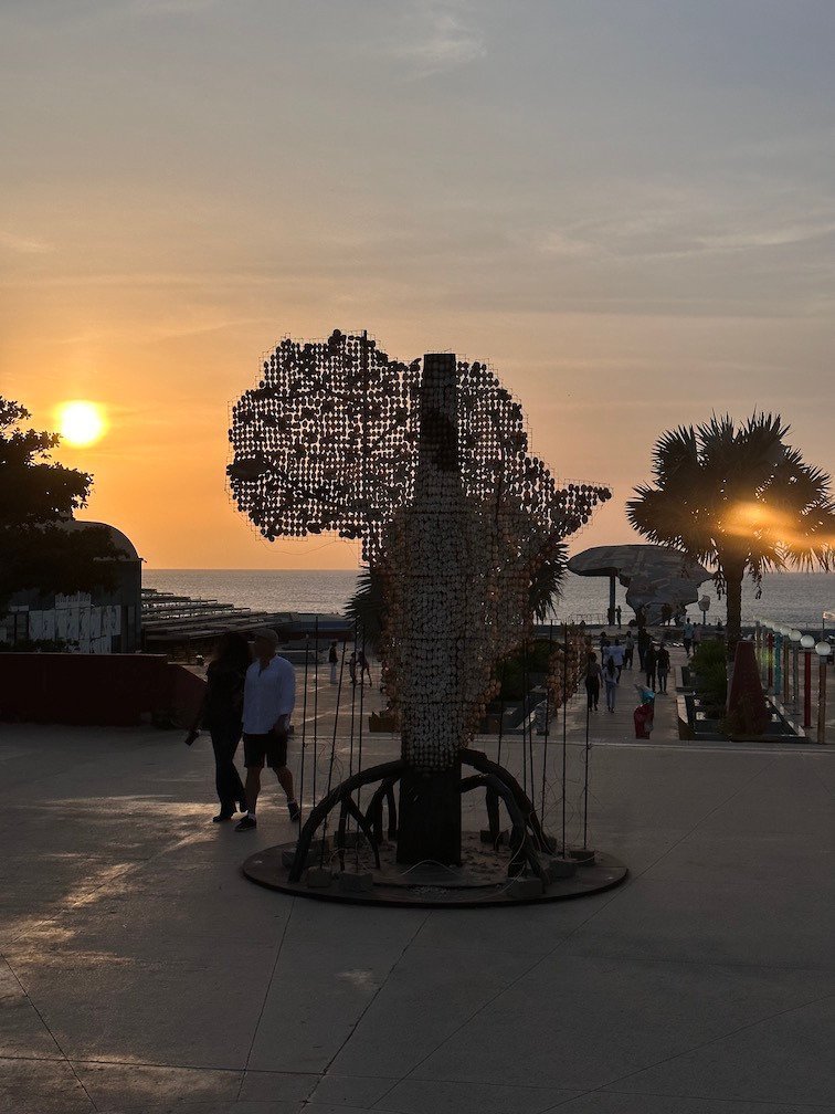 A metal sculpture shaped like Africa stands near the sea at sunset in Dakar.