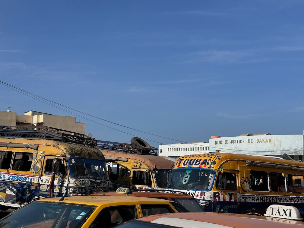 Painted buses and a yellow taxi stand at a bus station in Dakar.