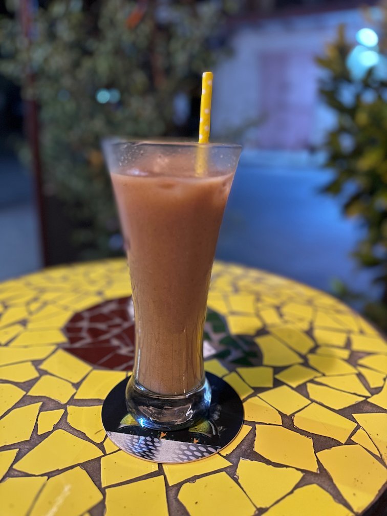 A tall brown drink with a straw stands on a mosaic table.