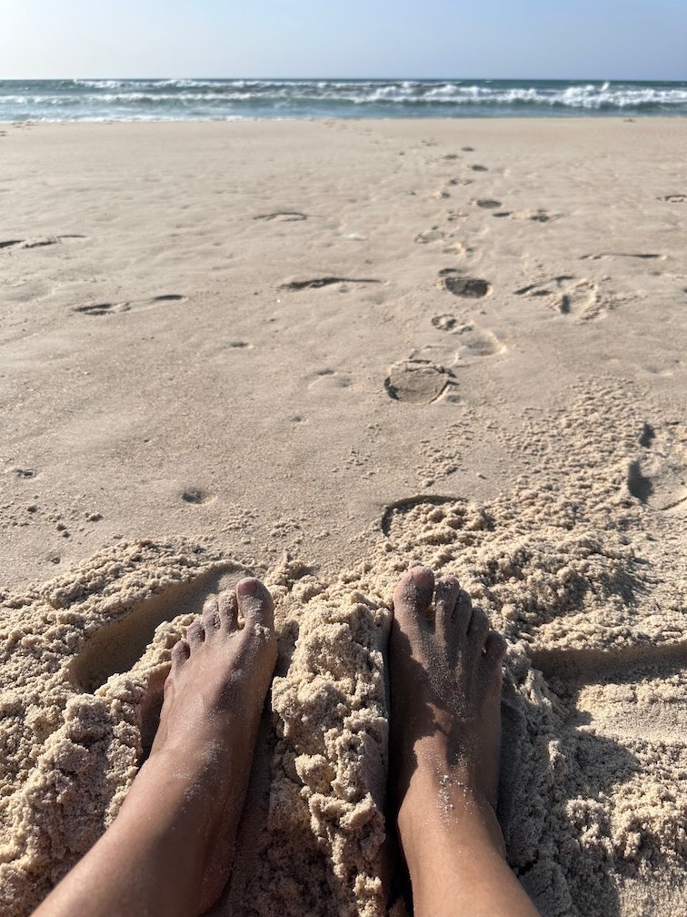 Bare feet rest in the sand of a beach near the sea in Dakar.