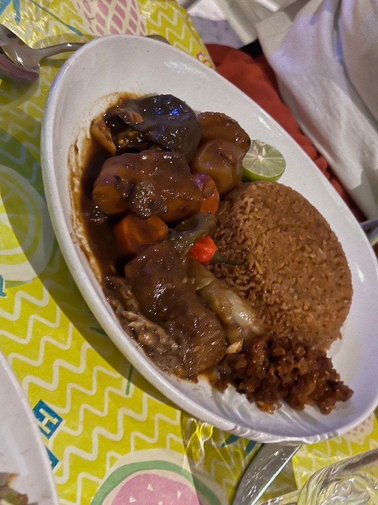 A plate of meat stew with brown rice stands on a colorful table.