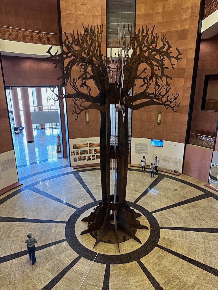 A large metal baobab tree sculpture stands in the round hall of a museum in Dakar.