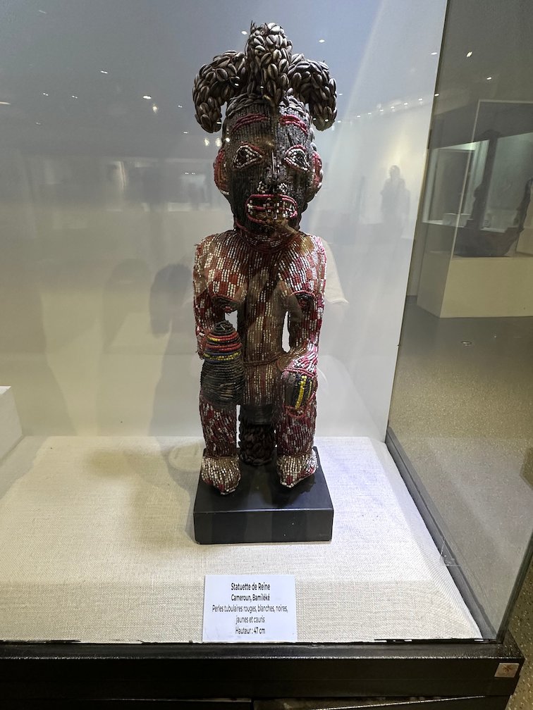 A carved and painted wooden figure stands in a glass case in a Dakar museum.