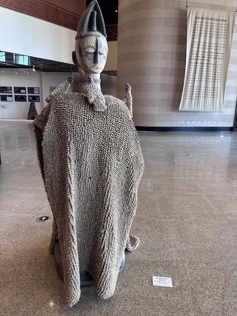 A tall ancestor statue covered in cowrie shells stands in a museum hall in Dakar.