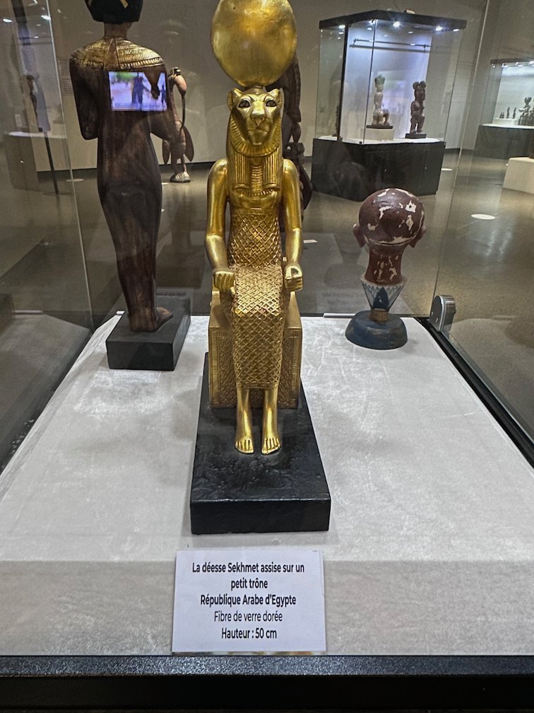 A golden seated statue stands in a glass case in a museum in Dakar.