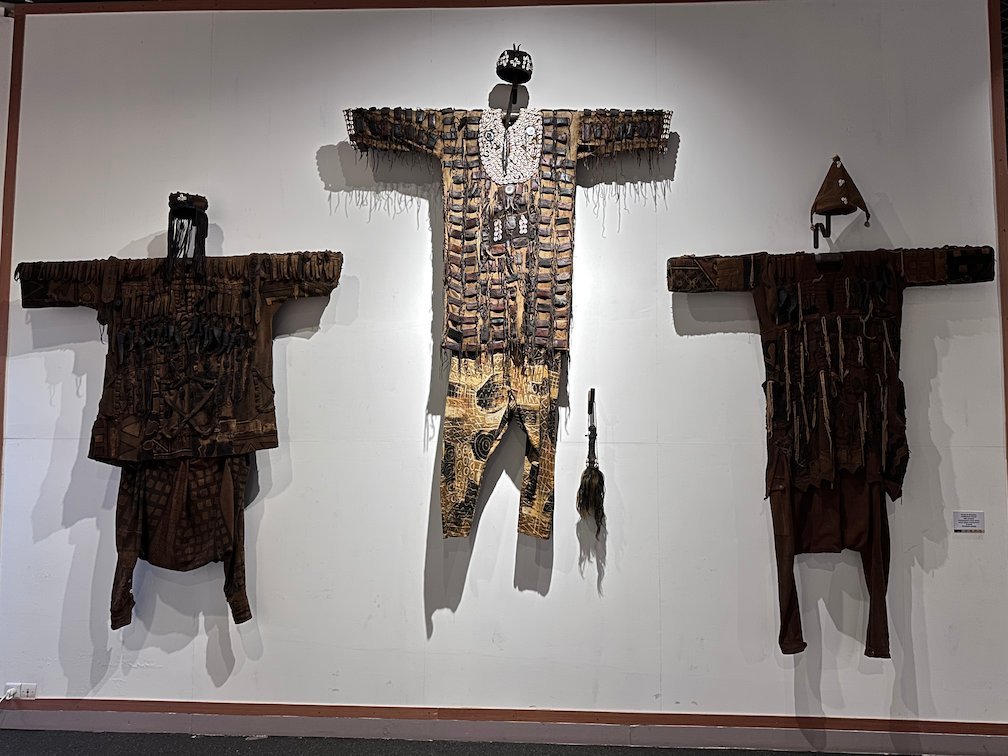 Three old ritual costumes hang on a white wall in a Dakar museum.