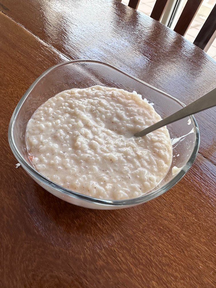 A glass bowl of creamy rice dessert stands on a wooden table.