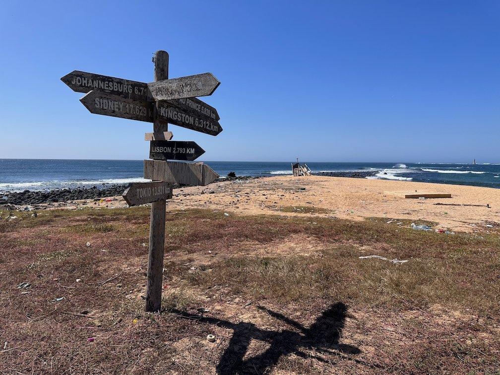 A wooden signpost with arrows stands on the coast in Dakar.