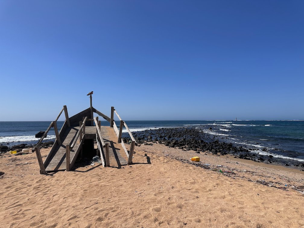 A wooden structure stands on the sand by the rocky coast in Dakar.