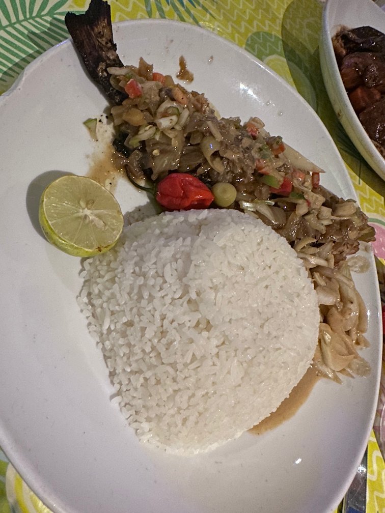 A plate of fish yassa with onions, rice and lime stands on a table.