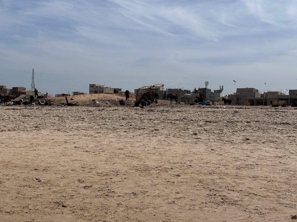 Carts and people stand on the wide sandy beach in front of buildings in Dakar.