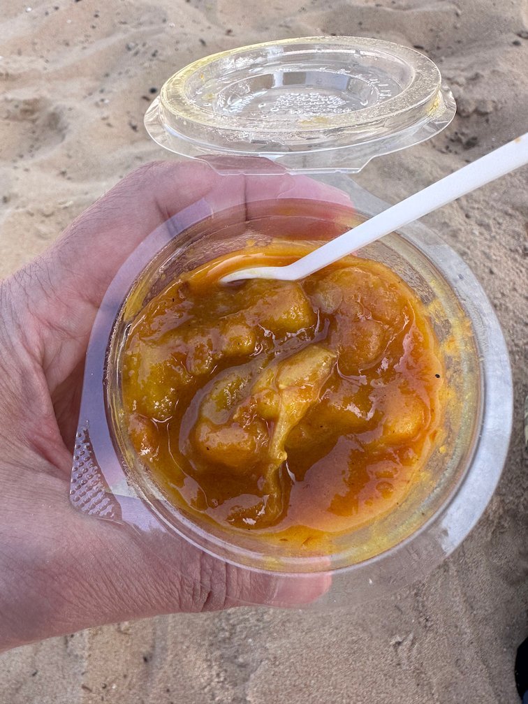 A hand holds a plastic cup of orange fruit on the beach in Dakar.